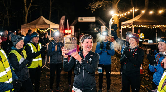 Five runners wearing head torches on an autumn woodland trail at dusk, passing glowing carved pumpkins during a Halloween night run.