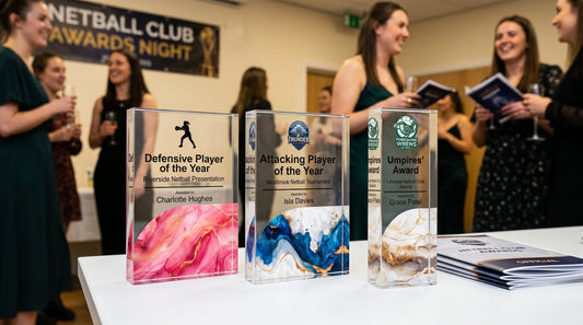 Three personalised netball trophies displayed at a club awards night, featuring Defensive Player of the Year, Attacking Player of the Year and Umpires’ Award acrylic trophies.